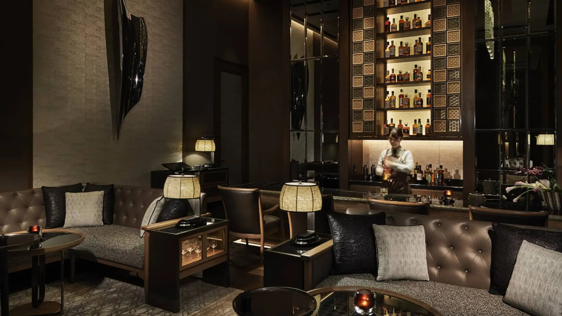 Bar Virty with dark coloured furniture, black wall art/sculpture and woman in uniform making drinks.