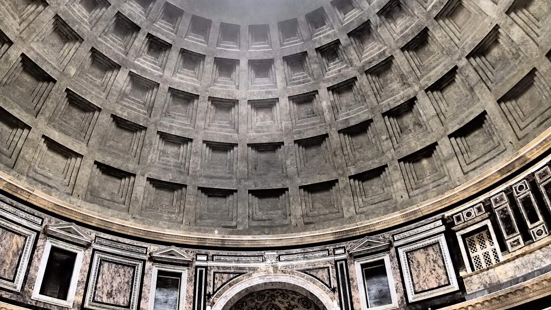 "Interior view of the Pantheon in Rome, showcasing its vast dome with the central oculus letting in natural light. The photo captures the grand columns, detailed sculptures, and the rich textures of the ancient walls, with visitors admiring the architectural marvel."