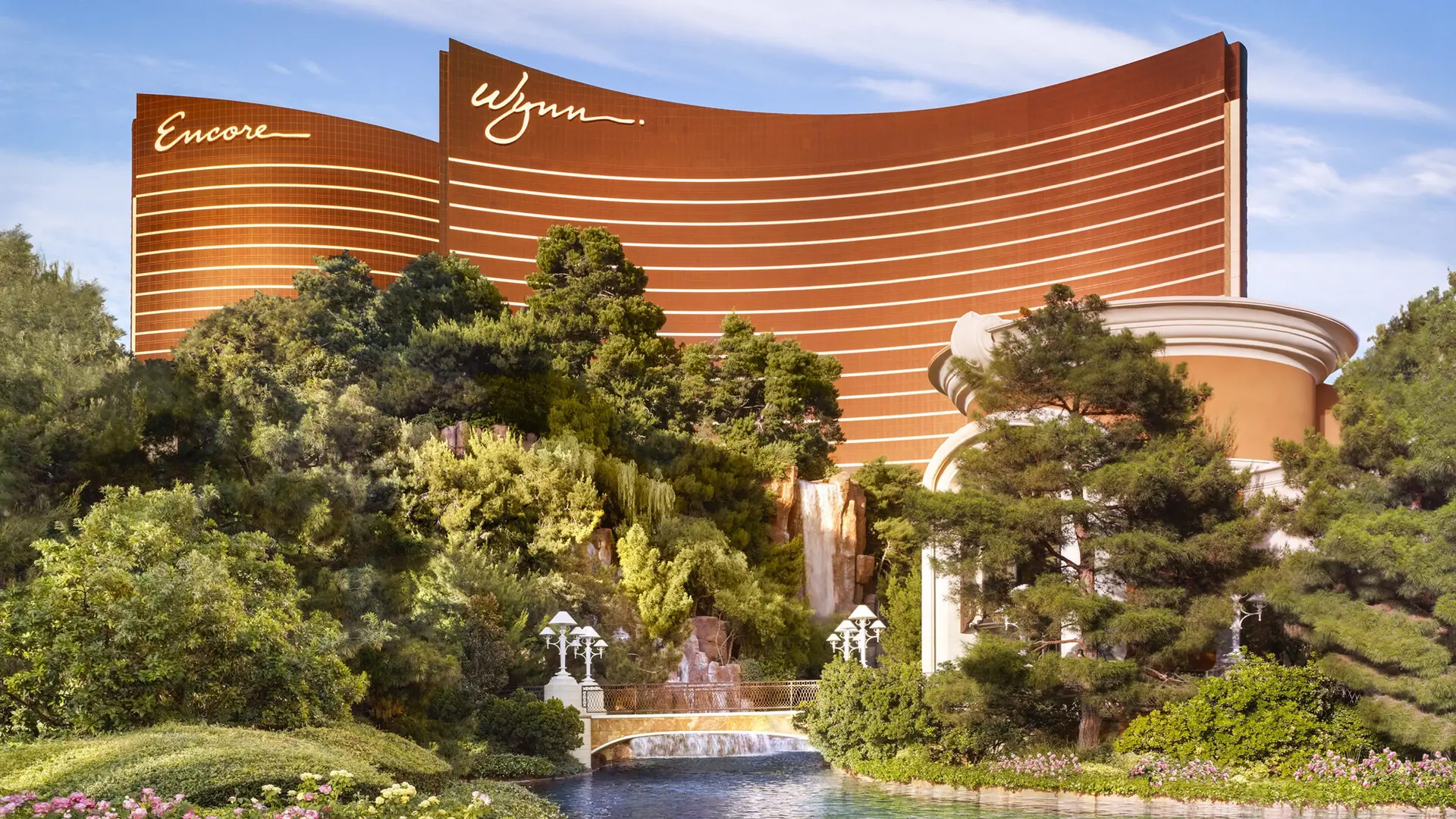 View of nature, gold and white bridge and the massive brown/bronze coloured building with white stripes saying: Encore and Wynn.
