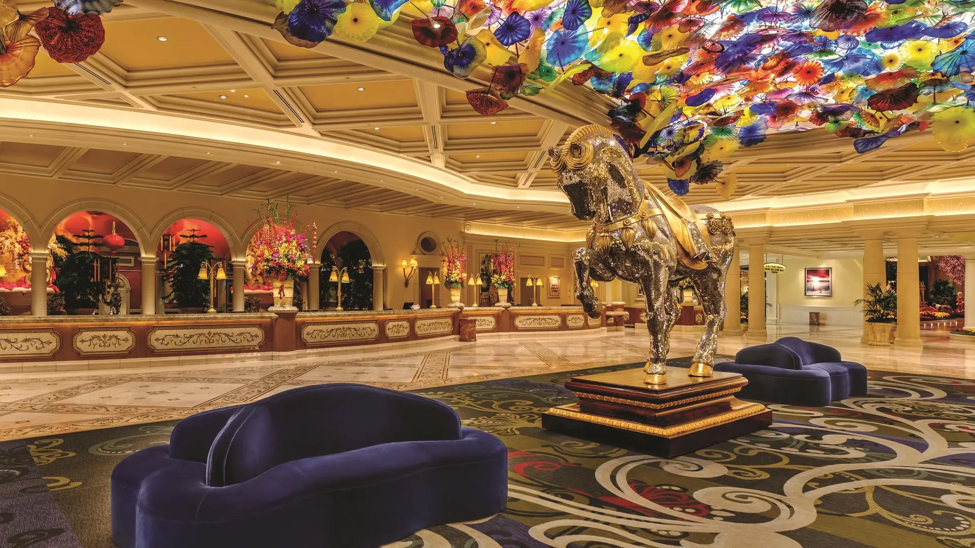 Massive lounge with two dark blue sofas, colourful carpet, and a golden and silver horse statue with colours in the roof.