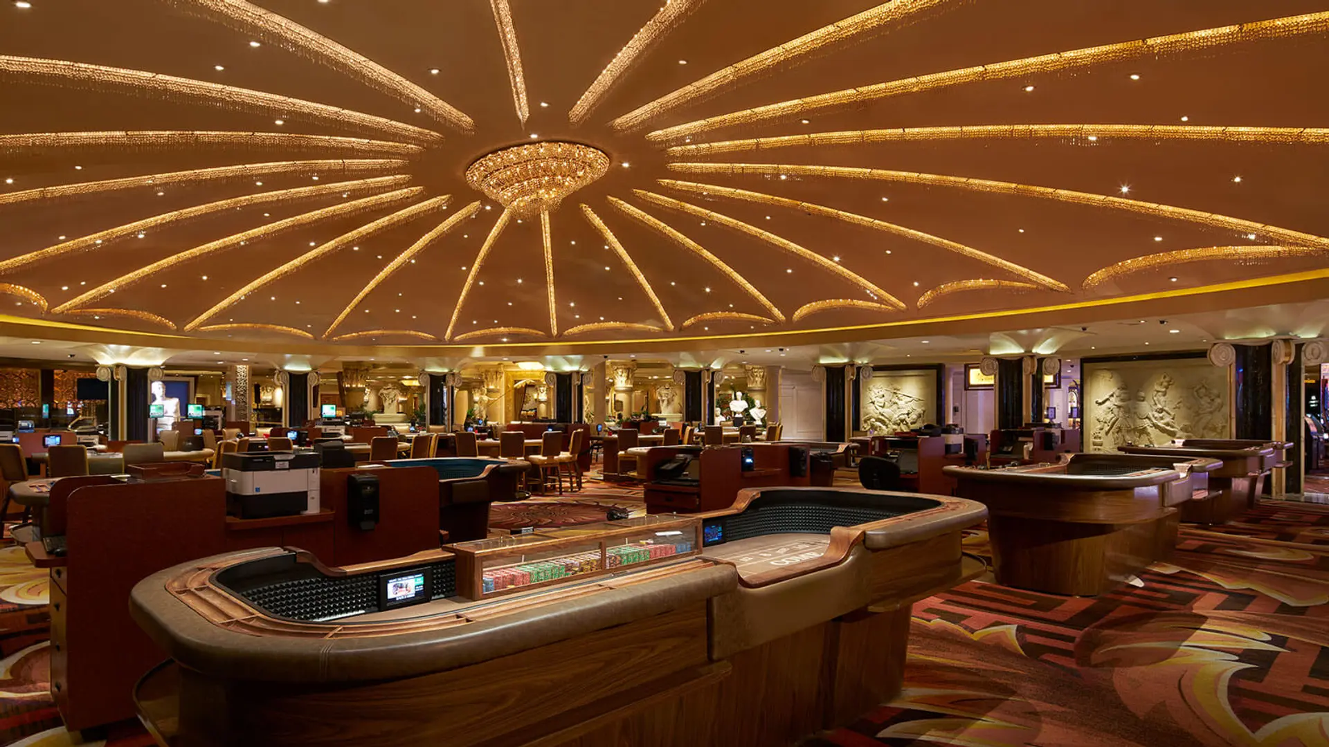 Casino with leather furniture, engraved statues in the walls, and a large golden lamp in ceiling.