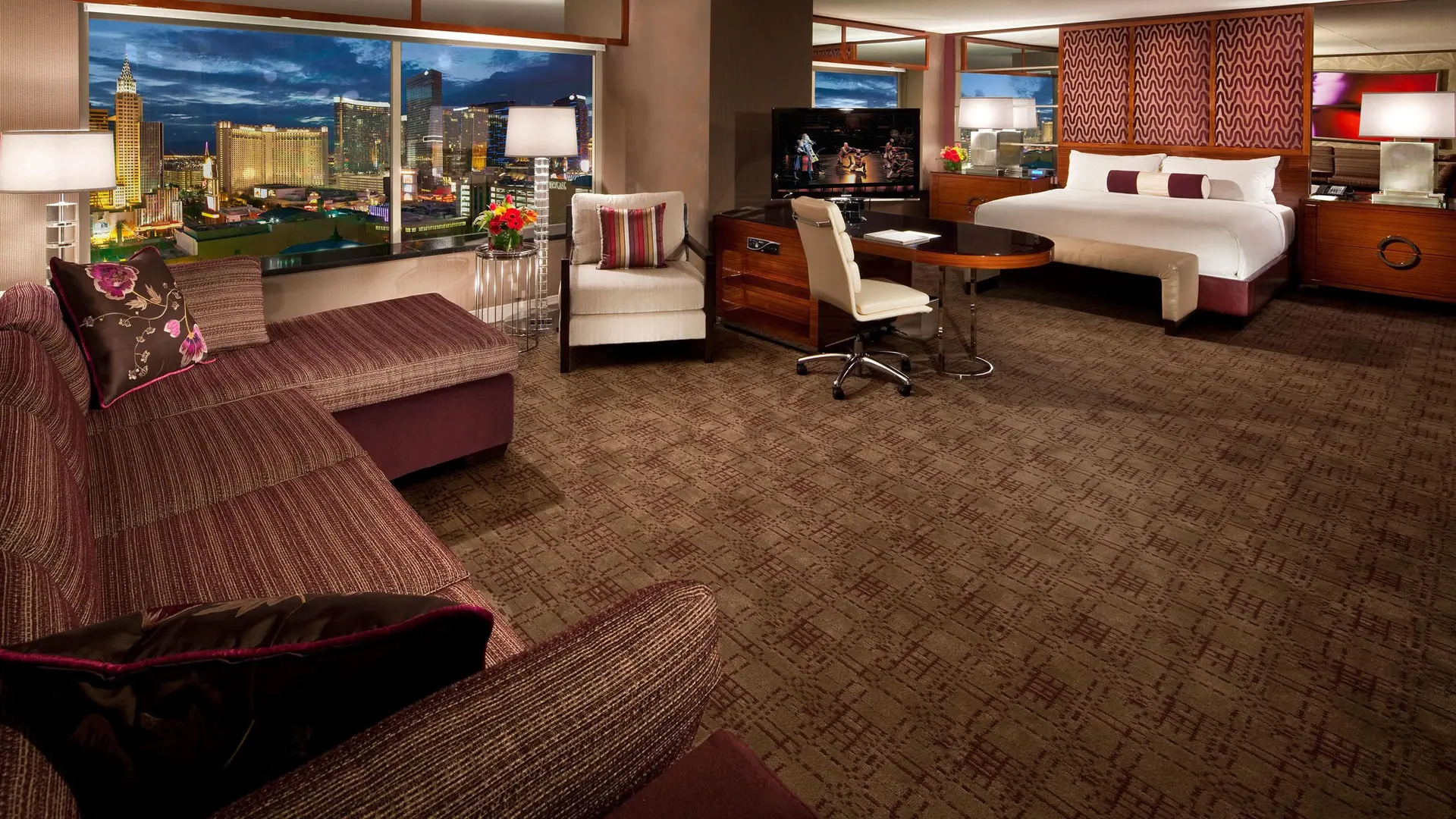 Room at the MGM Grand with red furniture, white beds, tv, and large windows showing the view of Las Vegas.