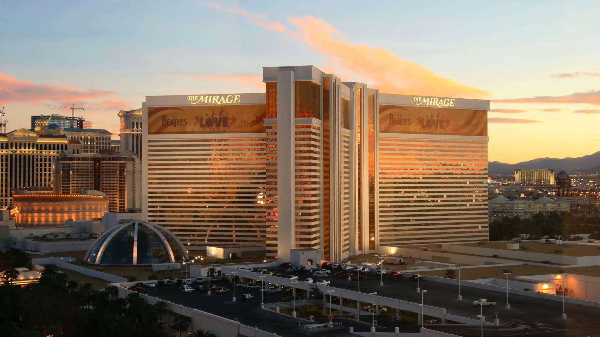 Large white and golden building with glass strips in vertical form, at the top of the building text saying: The Mirage in gold on white and under the text advertisement for The Beatles and text saying LOVE.