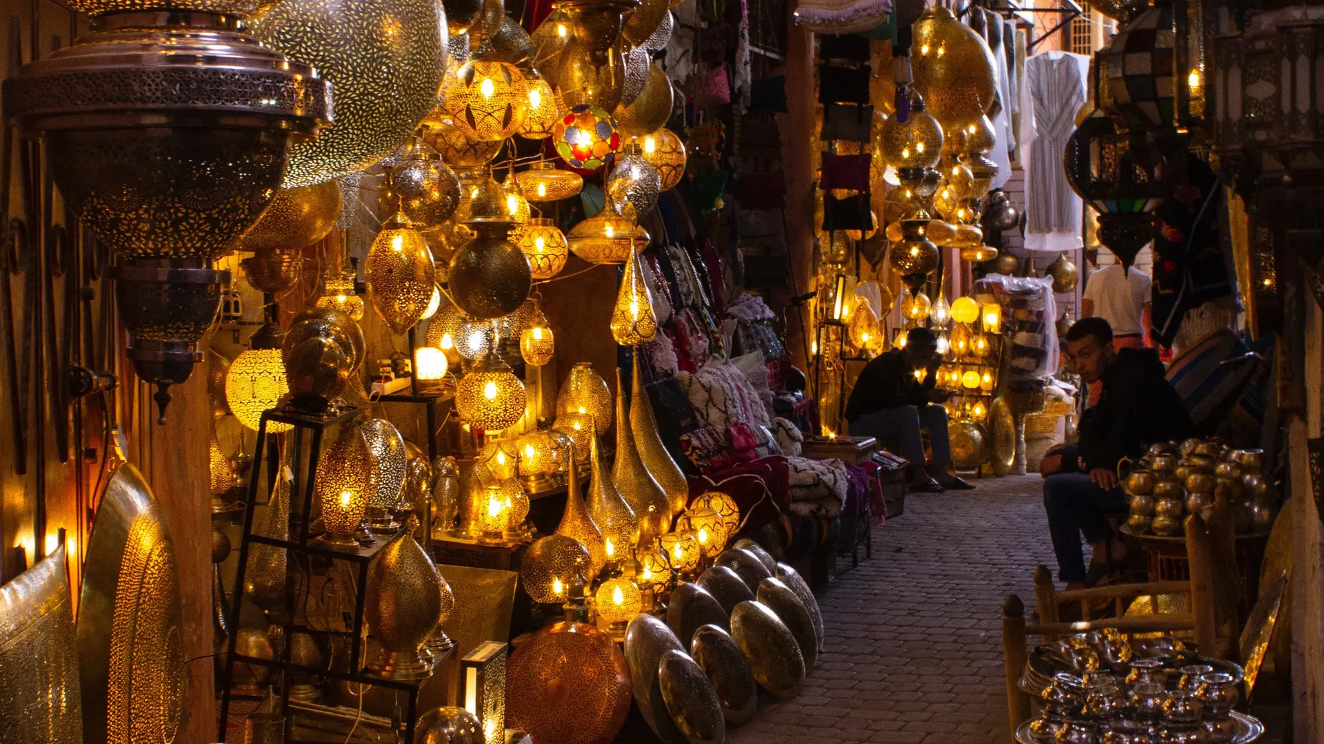 Moroccan market with man y lamps and lanterns with two people sitting.