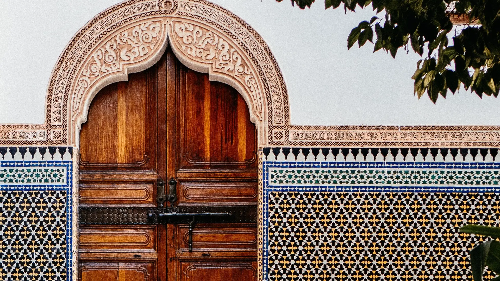 A large wooden door with polished clay tiles walls making a pattern of yellow, blue, white, black and pink.