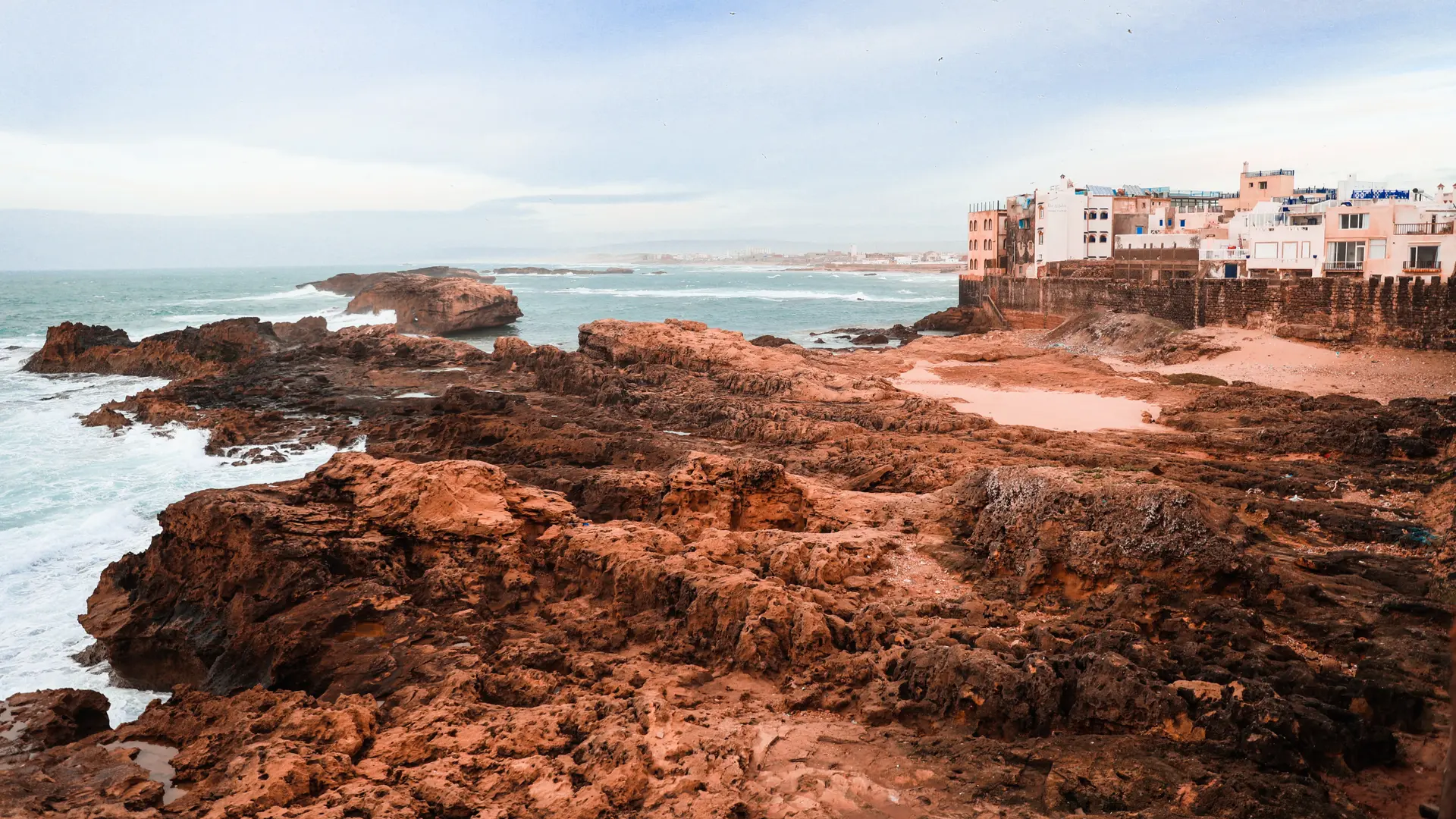 A rocky coast with the ocean slamming against the orange rocks.