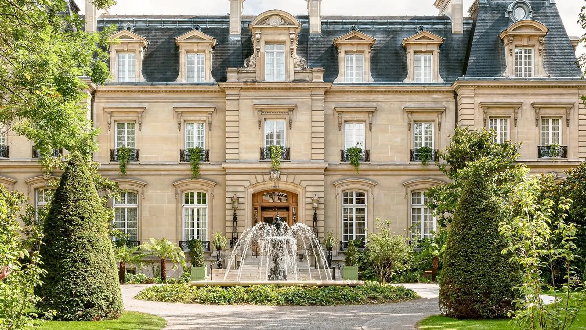 Outside of saint james paris with a fountain infront of the main entrance surrounded by plants and trees