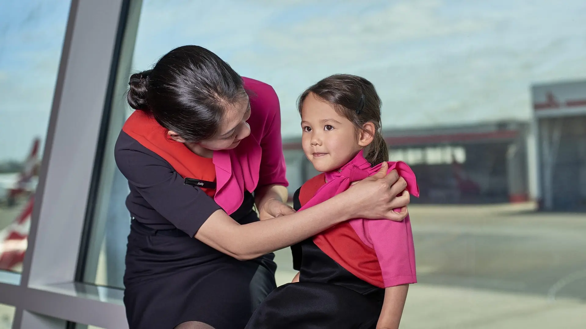 Young girl in pink being taken cared of by a flight attendant before the flight.