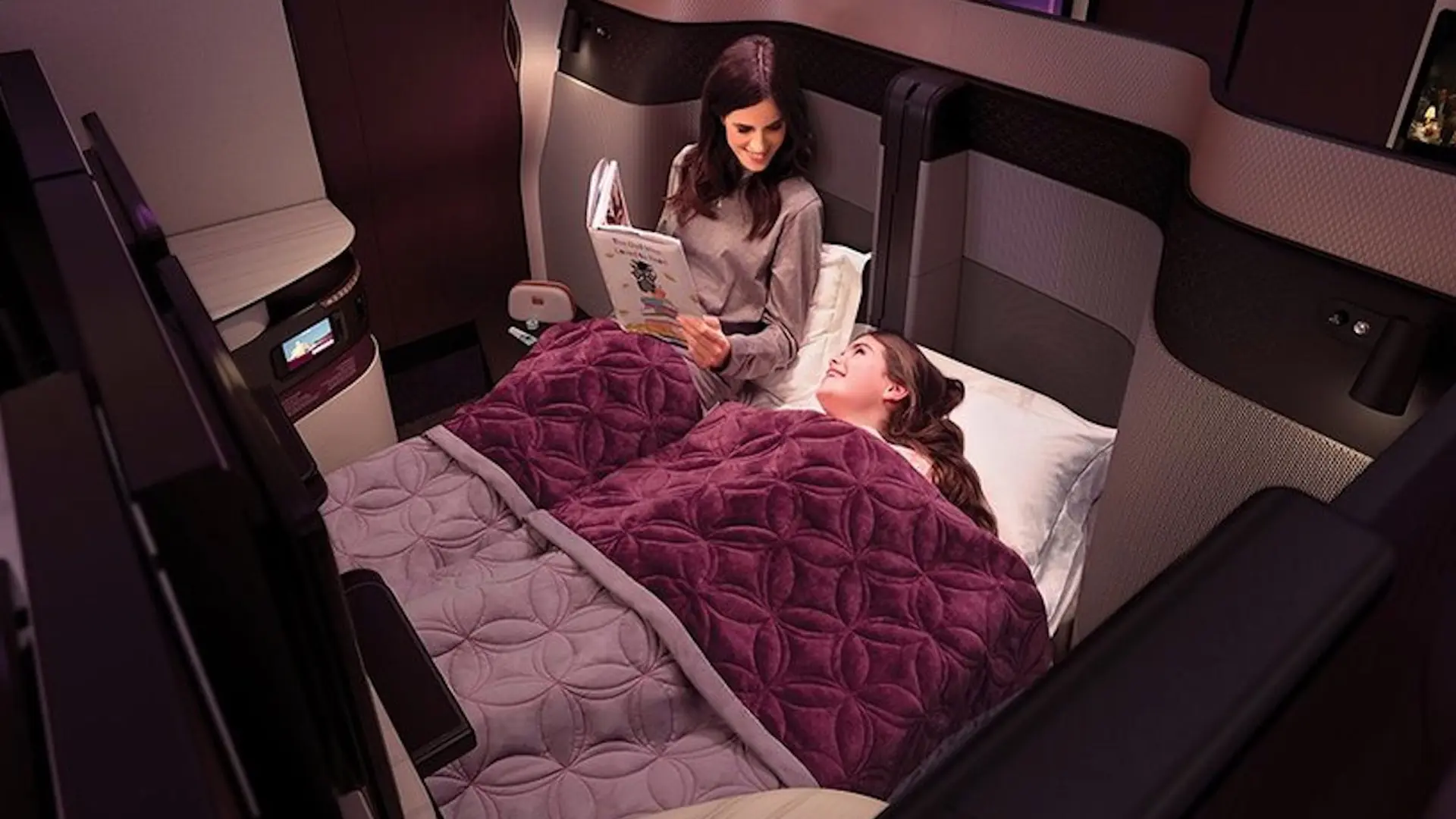 Happy woman and her daughter getting ready for sleep at a businessclass flight with a purple carpet over them.