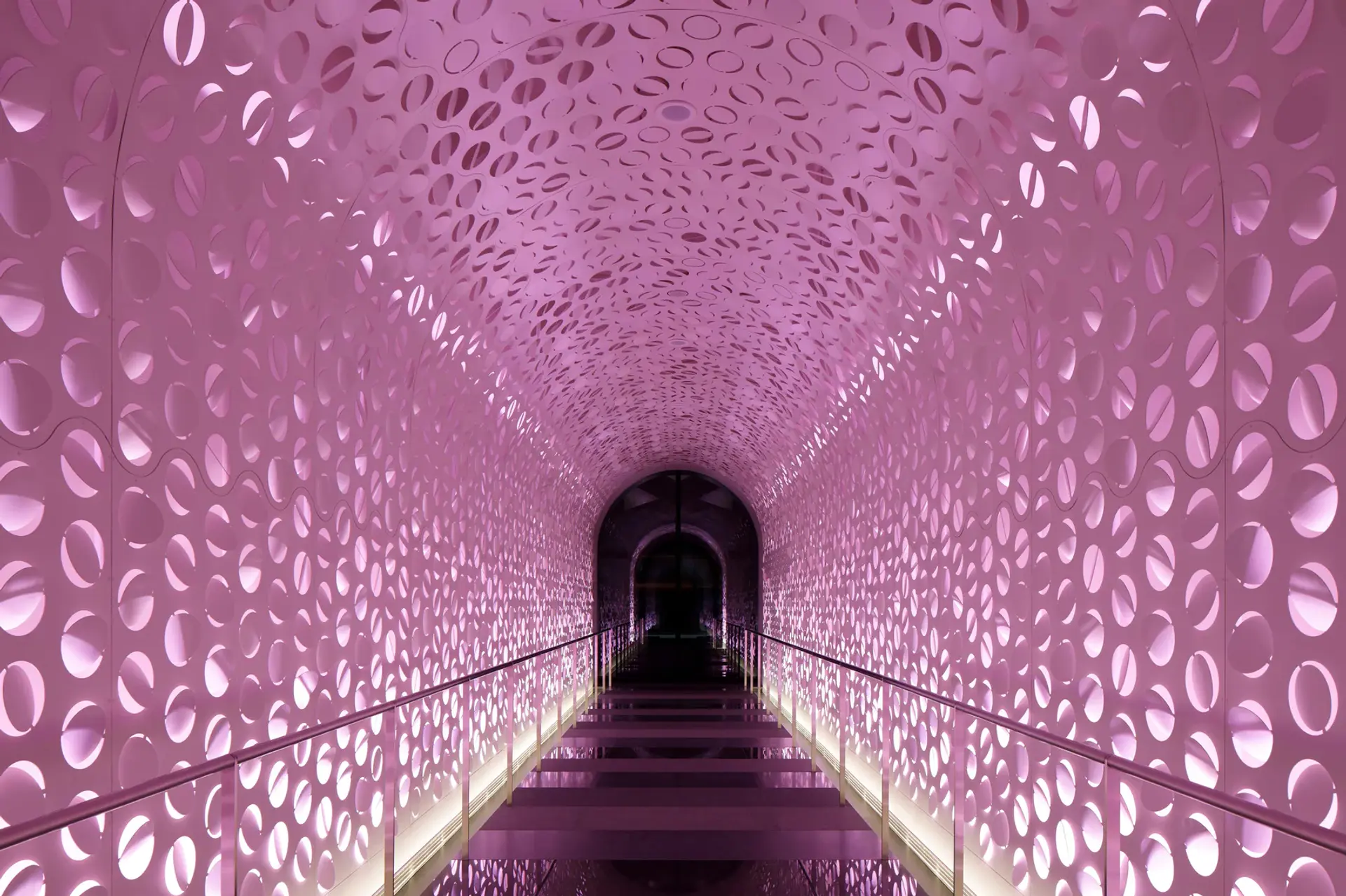 Corridor with pink lighting as walls and roof and a  black walkway 