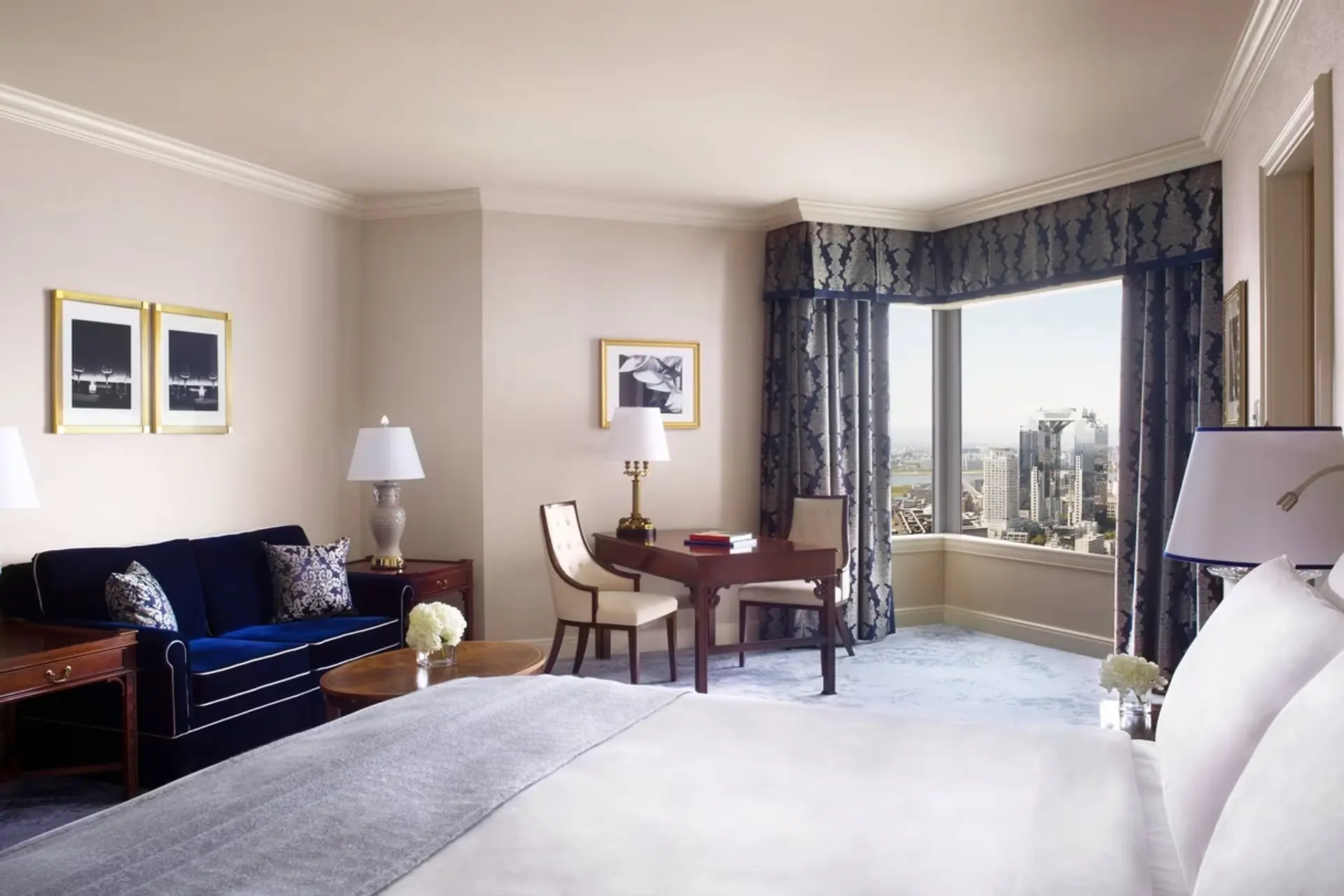 White kingsize bed, blue sofas, brown table, and view to Osaka at The Ritz-Carlton in Osaka.
