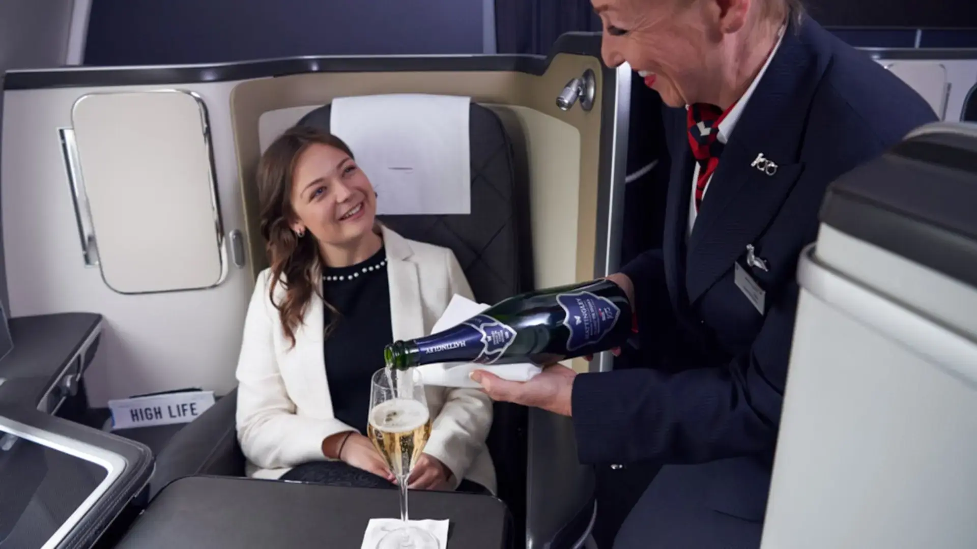 an air hostess serving champagne to a woman in british airways first class
