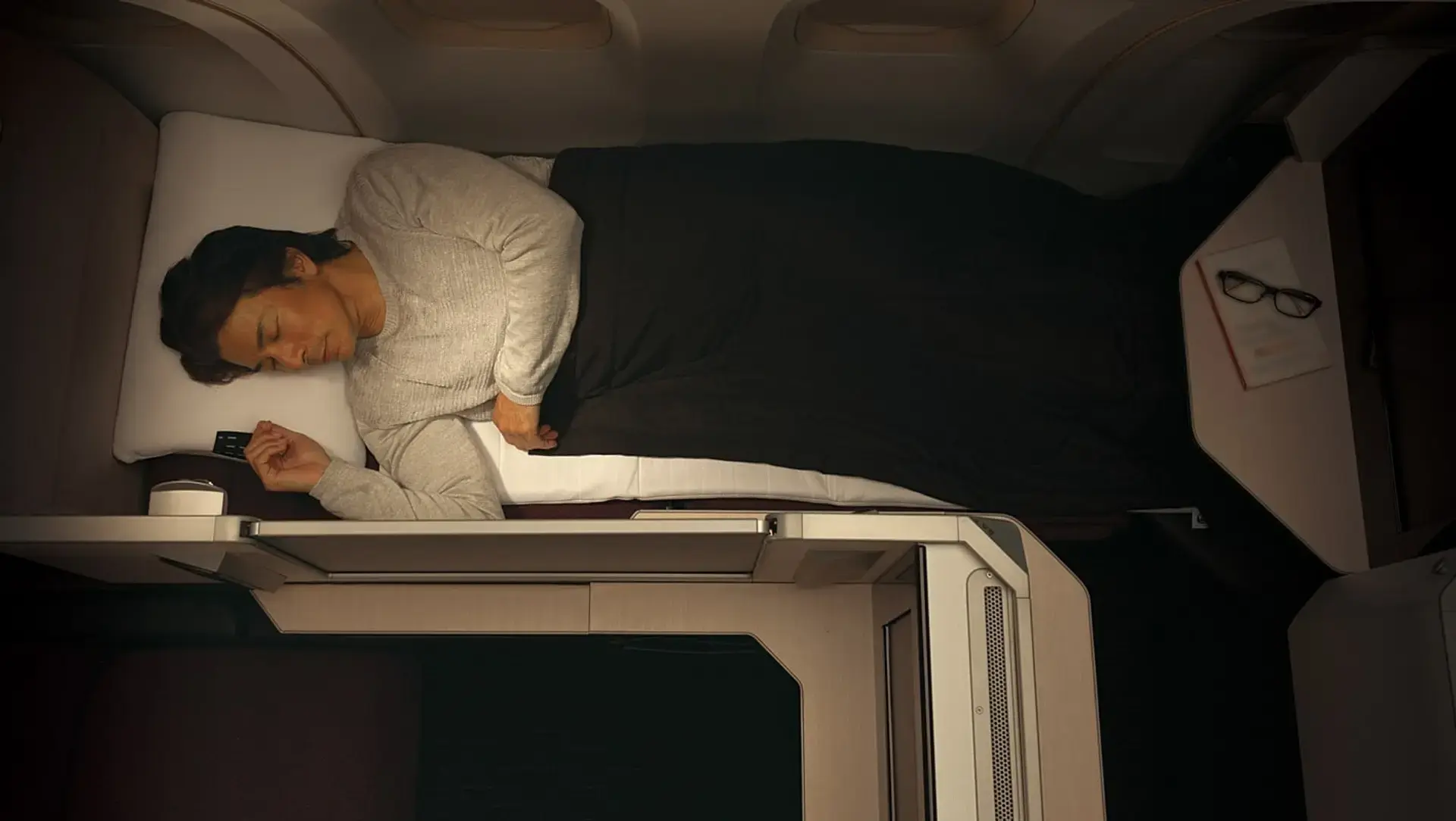 a man sleeping in his fully reclined JAL SKY SUITE Seat