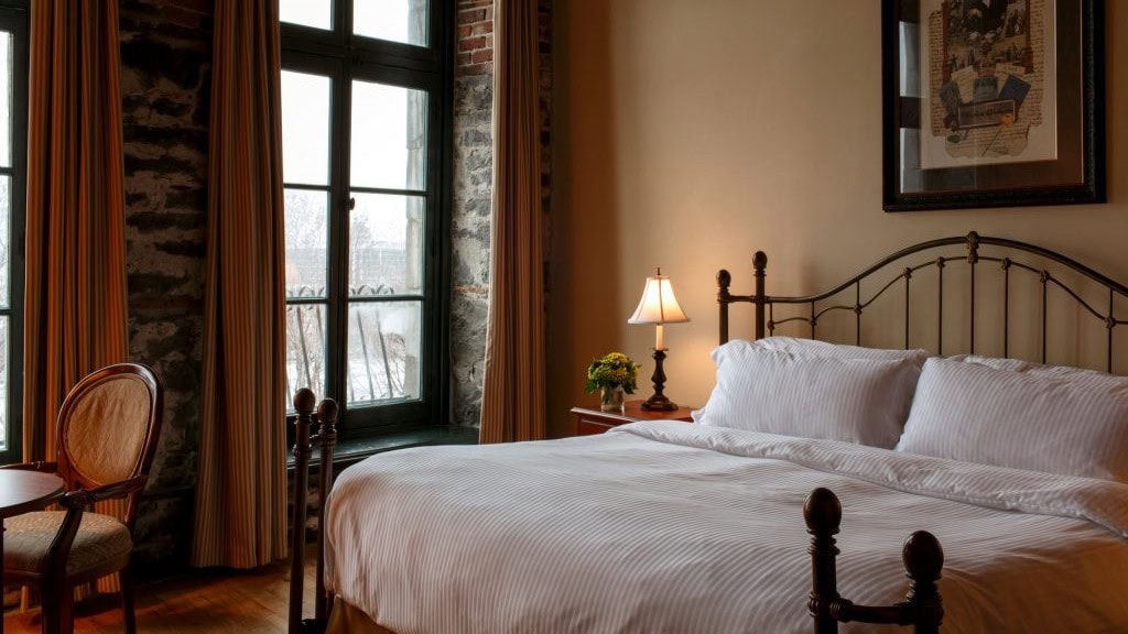 Bedroom with white bed, tender lightning and a panting at Auberge de Vieux port Montreal