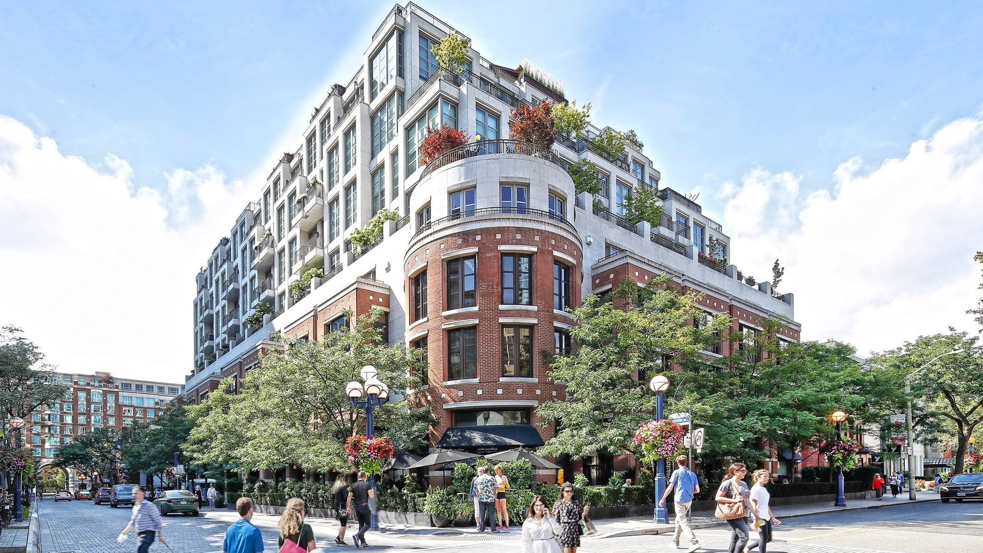 The outside of the hazelton hotel toronto made of brick and glass windows with people walking on the street