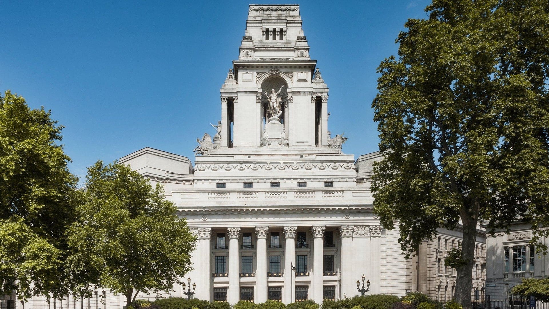 Outside view of Four Seasons Hotel London witch has a white palace design, roman inspired statues and white brick design.