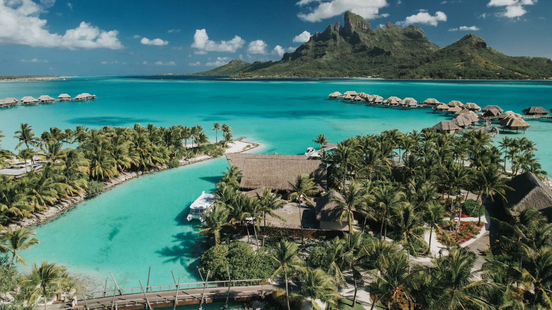 Bird perspective of the Four Seasons Resort, Bora Bora with beautiful clear water, palmtrees, large cabins stretching out to the water.