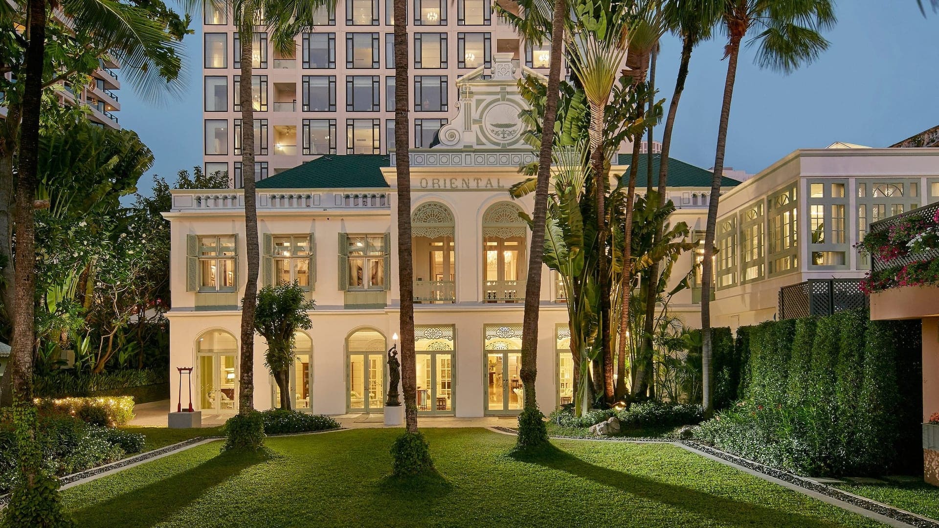 Garden view of Mandarin Oriental Bangkok, Thailand with tall palm trees and classical white design and large windows to the garden.