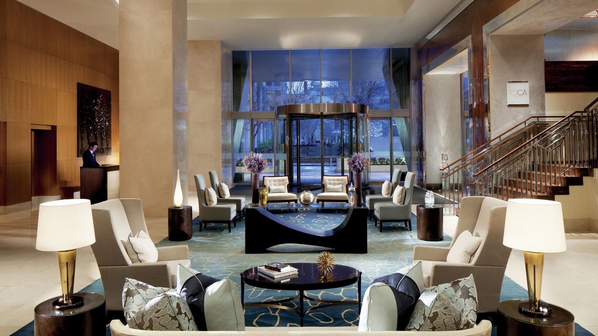 The reception of the ritz carlton hotel toronto with white chairs and desk on the left side with a reception worker behind