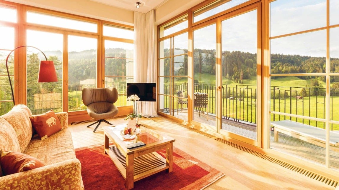 A relaxing area with a couch, tv, a red carpet with big windows with a view of Green thick forests.