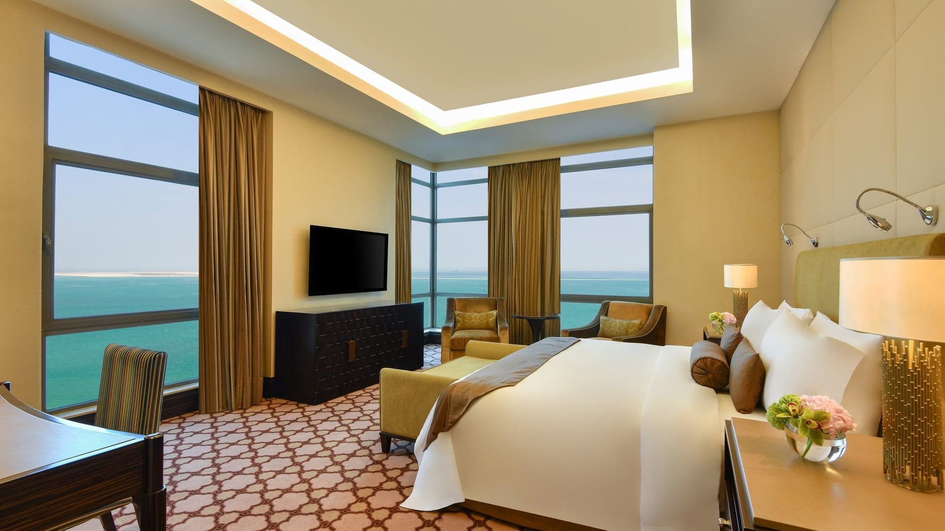 Hotel room at St Regis Doha, with beutiful view of the ocean,television screen, kingsize bed, lounge chairs, working chair and bedside table.