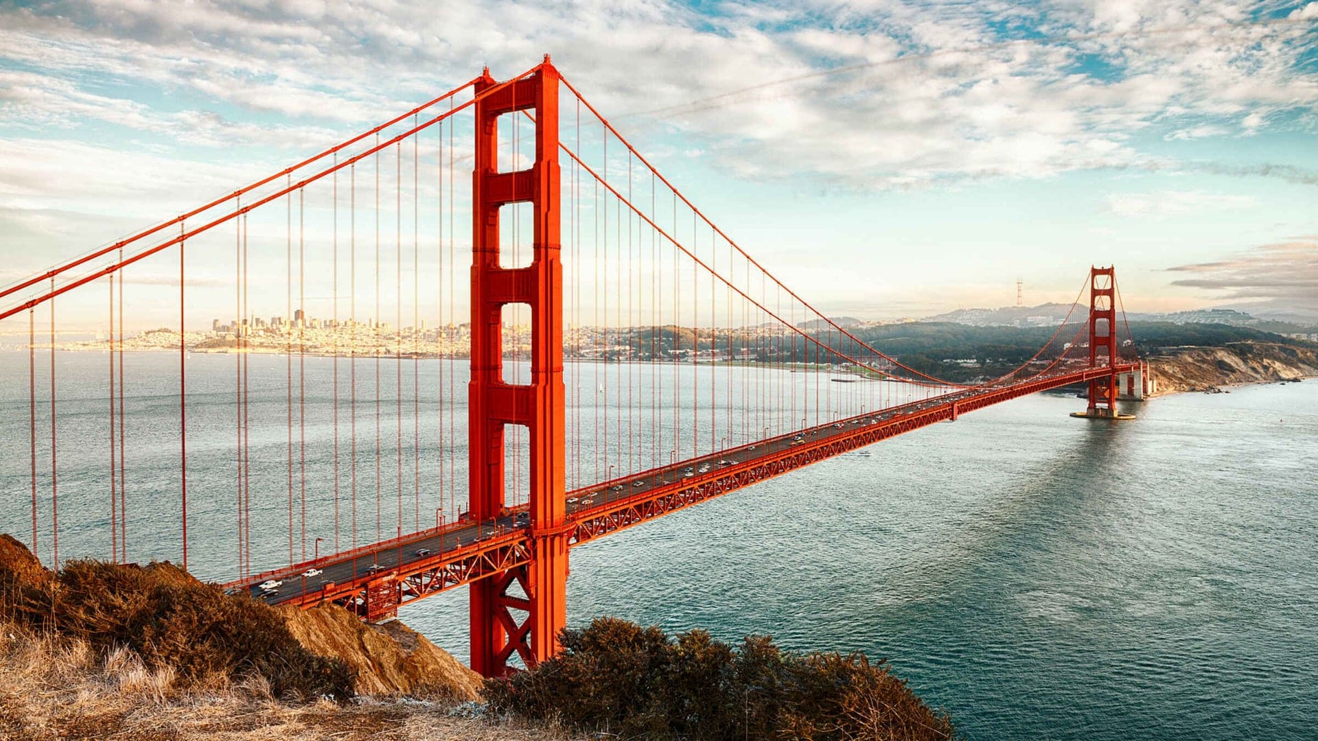 The large, red, long and water and nature surrounded Golden Gate Bridge in San Francisco.