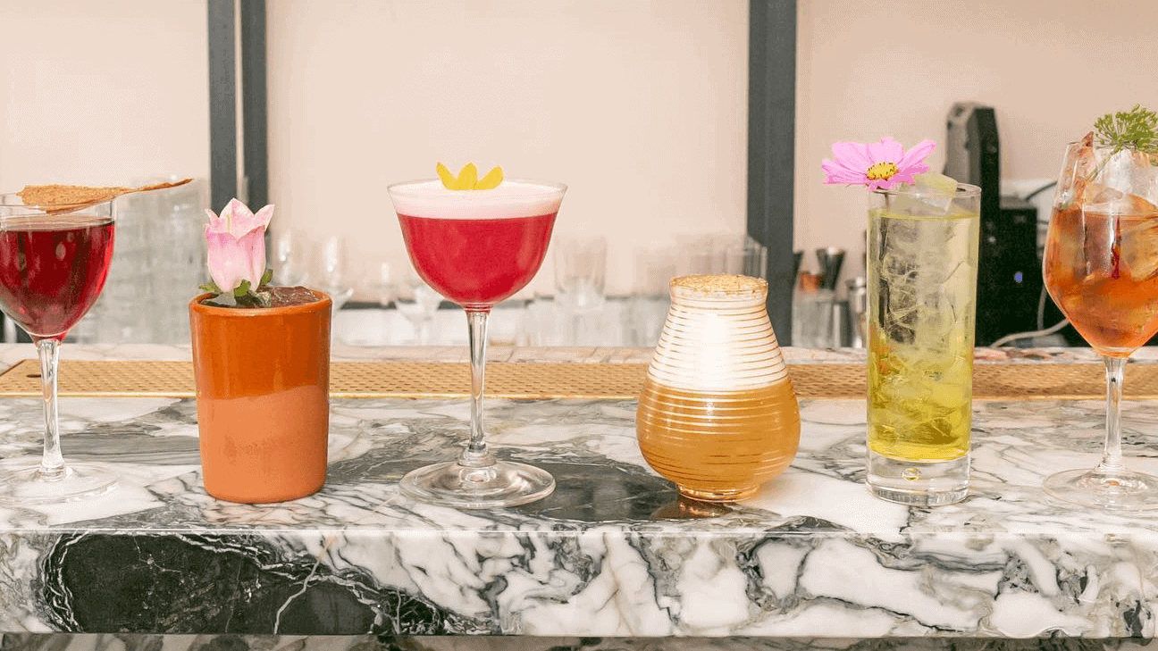 Red wine, flower pot, drink in red, and yellow standing on top of a marble table.