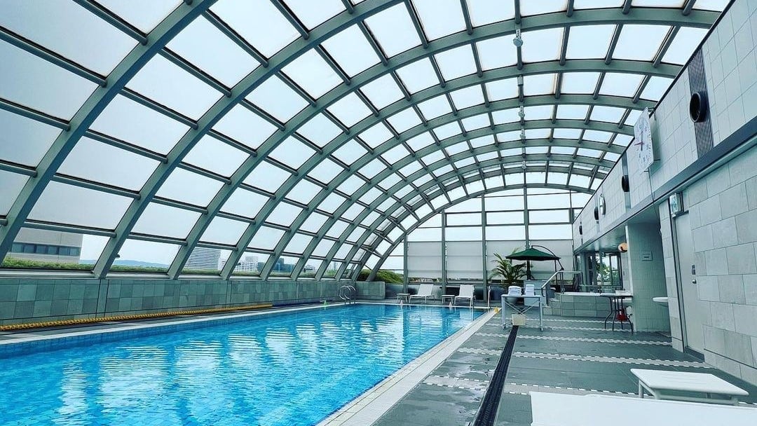 Pool area with window rooftop, sunbeds and clock.