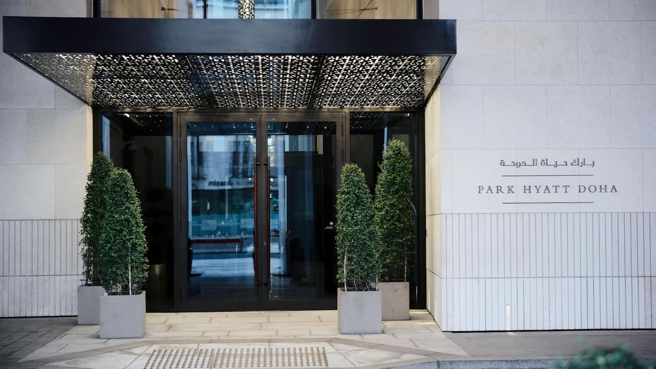 View of entrance to Park Hyatt Doha with beautiful plants and large black entrance doors.