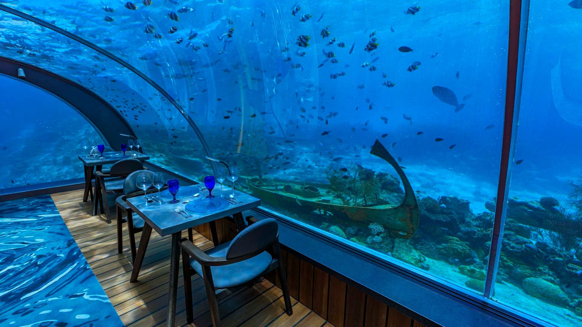 Underwater dining with wooden floor, blue furniture and glass walls and water view at Hurawalhi Island Resort in Maldives.