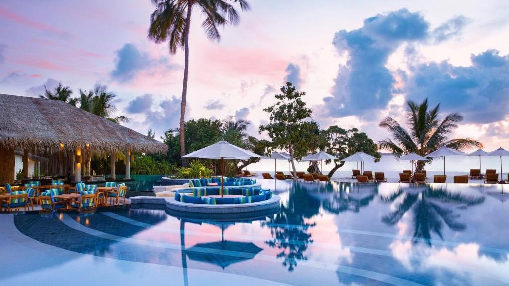 Pool area at Six Senses Laamu at evening time in Maldives featuring palmtrees and seating area.