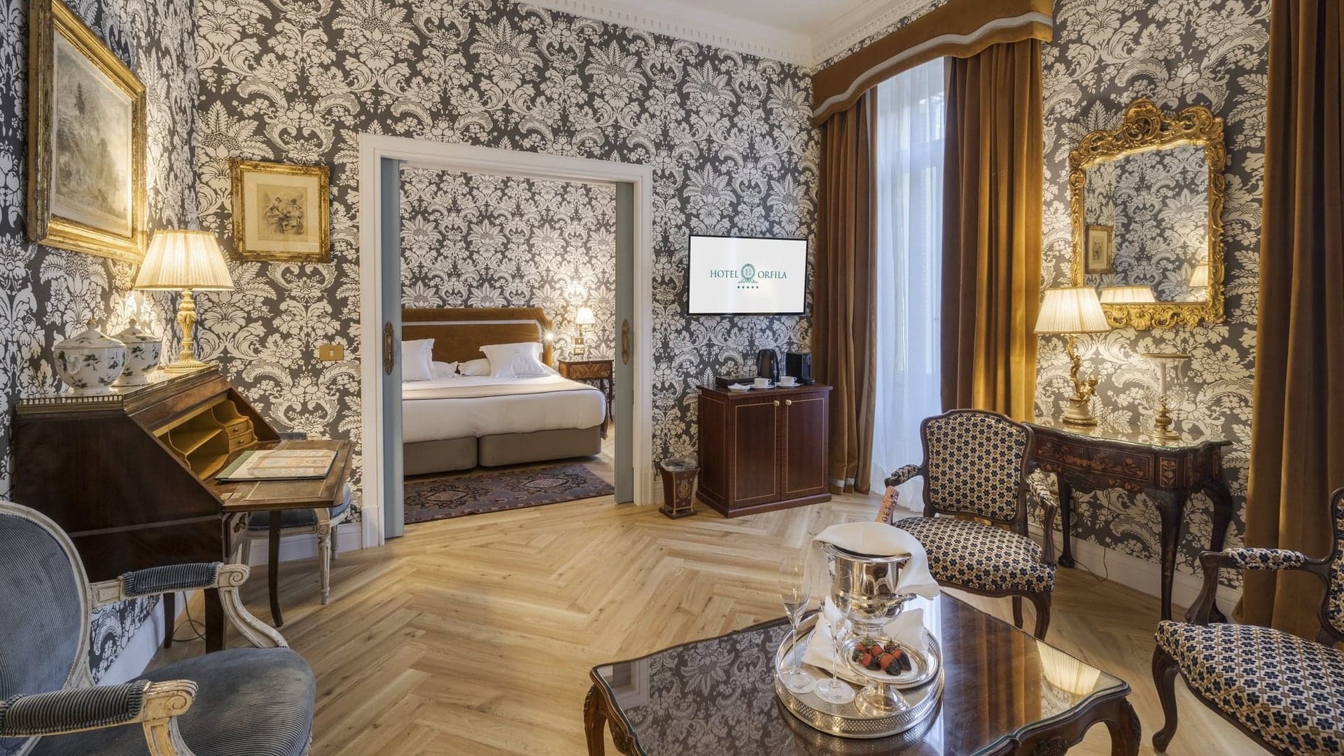 Hotel room with patter walls, wooden floor, flatscreen tv and entrance to the bedroom at Relais & Châteaux Hotel Orfila in Madrid