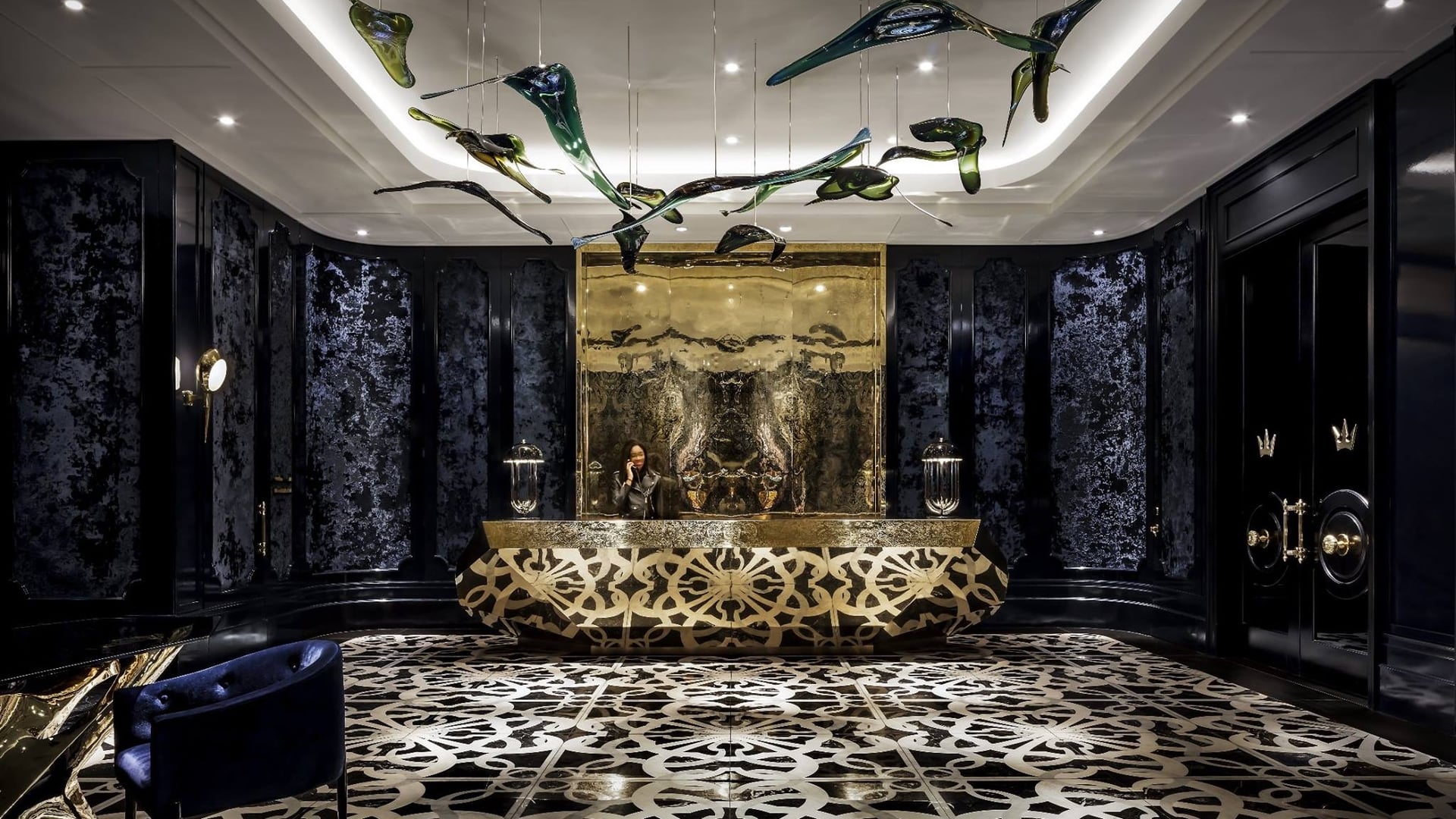 The reception of bisha hotel toronto with black, blue and gold decor and a lady standing behind the counter