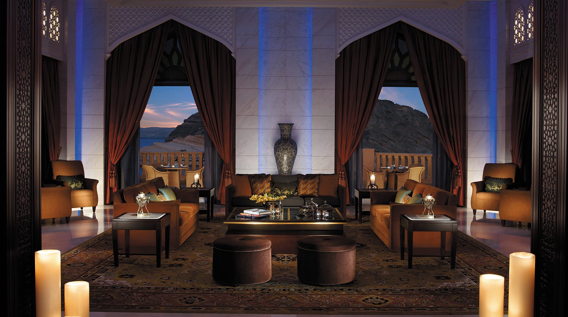 Living room  with brown sofas, marble walls and large windows out to beutiful mountains and oceans