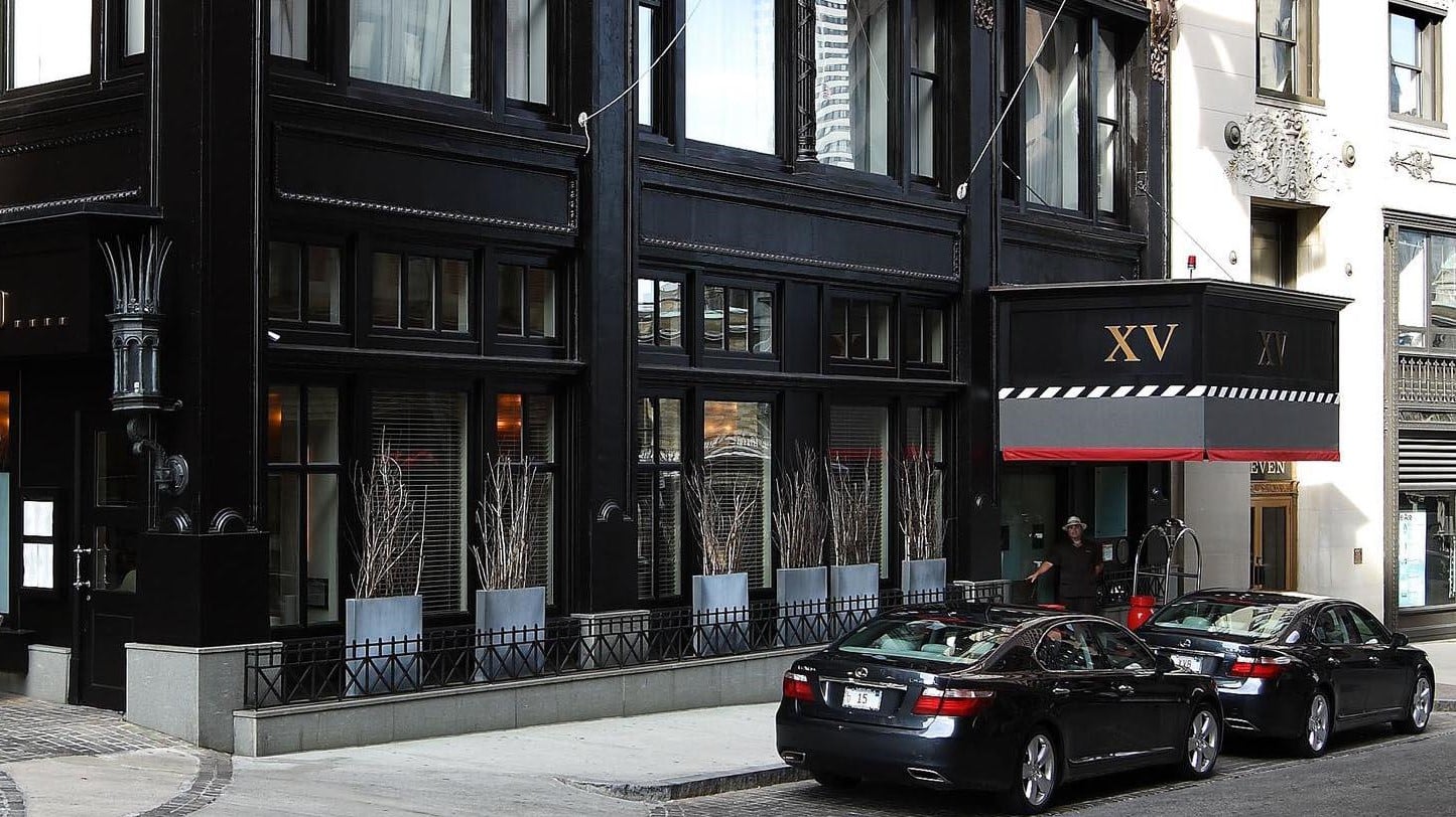 The outside of a all black hotel XV beacon with XV written in gold and two black mercedes parked upfront.