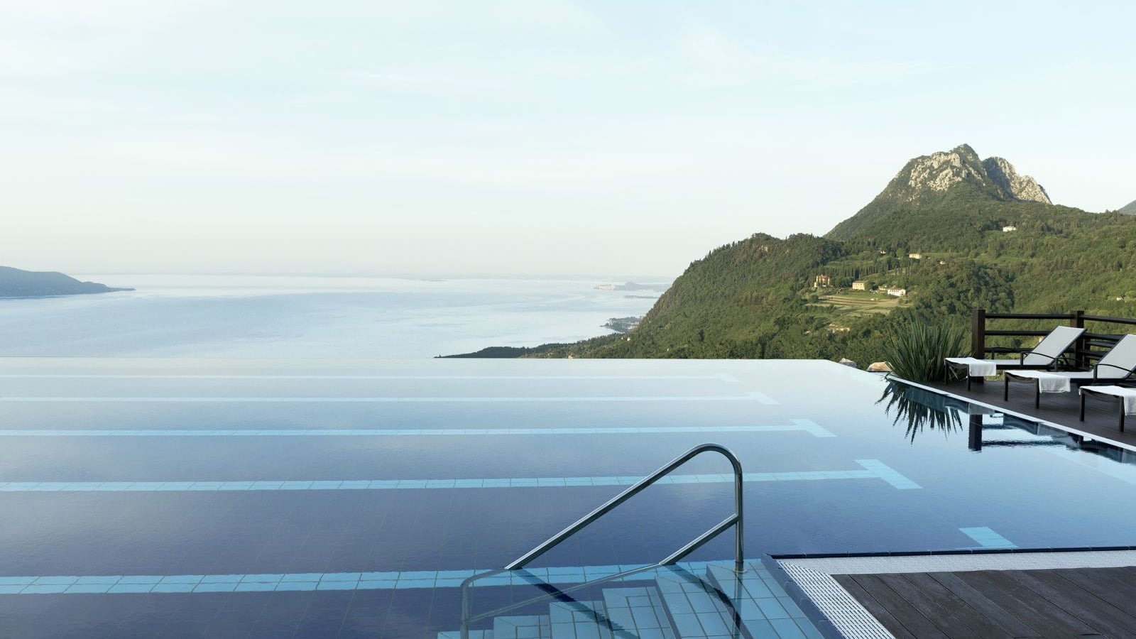 A outdoor infinity pool with a view of the sea and a cliff with a thick green forest