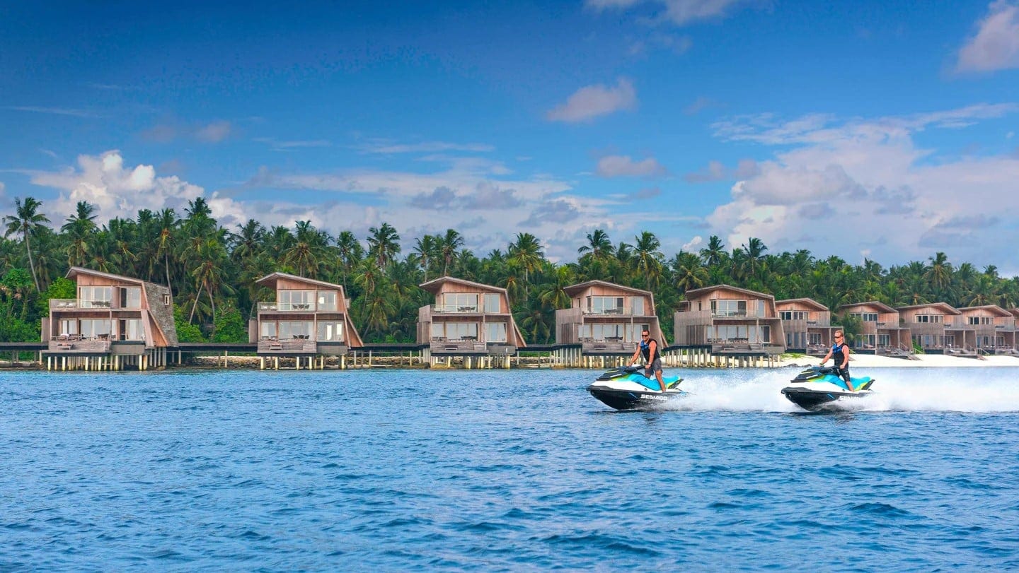 Two men riding jetski around The St Regis Maldives Vommuli Resort.