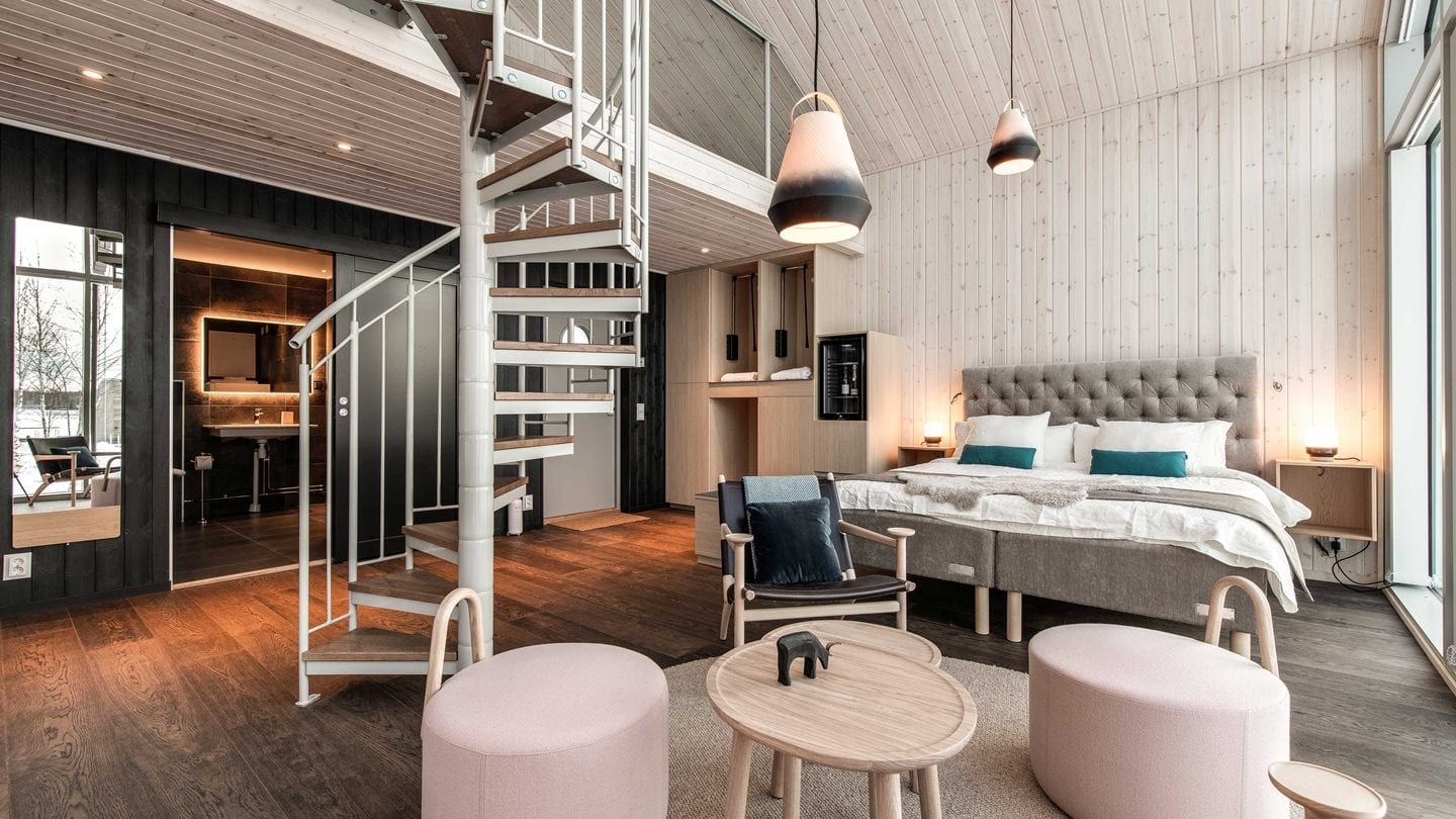 A room with a king sized a bed a back finished bathroom and a white staircase.