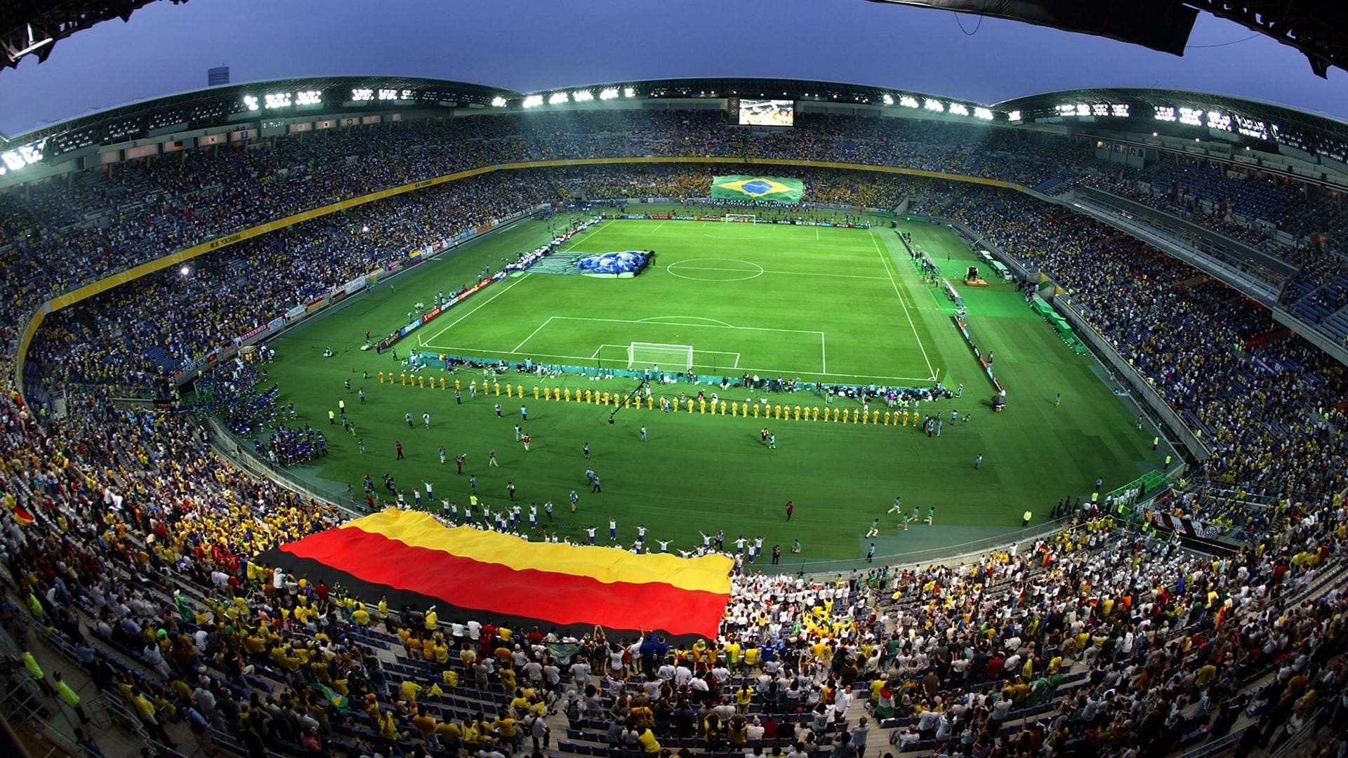 Soccer arena with the Spanish flag and Brazzilian flag and a lot of people watching.
