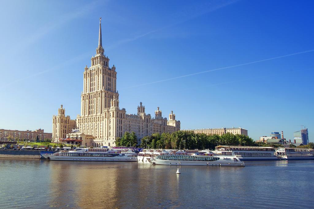 View from the water of Raddison Royal Hotel with two large white boats, and the large Raddison Royal Hotel in Moscow with a beige white design at a whopping 198 meters.