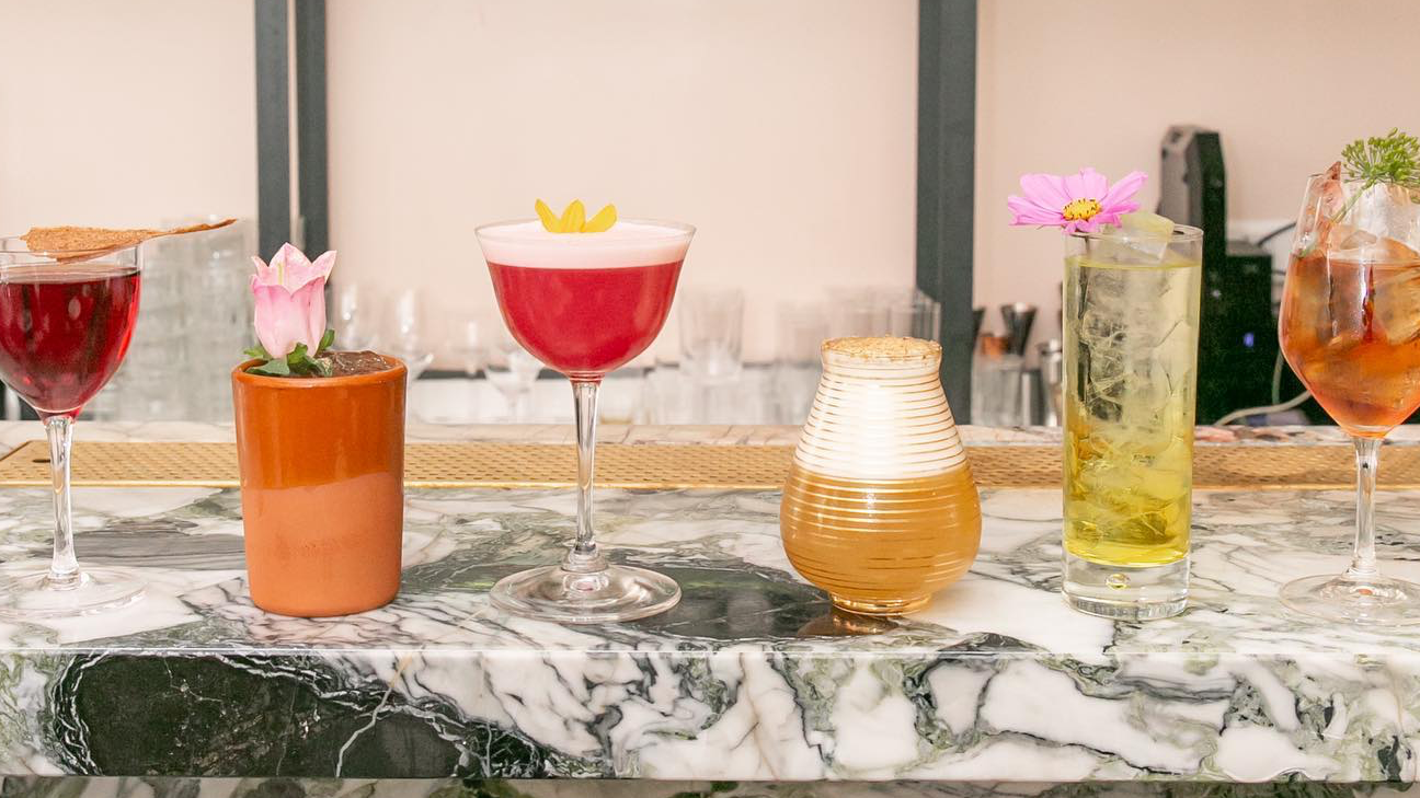 Red wine, flower pot, drink in red, and yellow standing on top of a marble table.