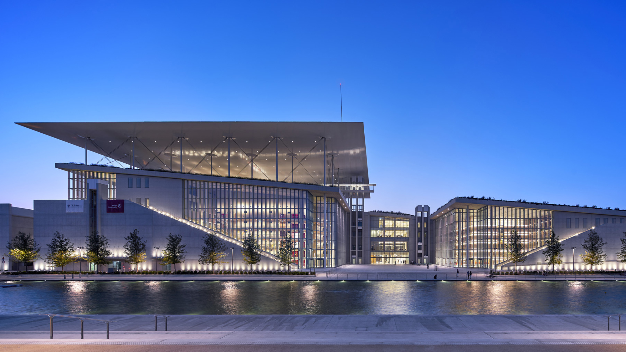 A modern cultural center by the water made of white stone with many glass windows.