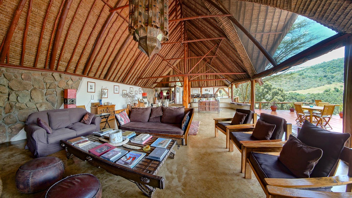 Large lounge with books, art, leather chairs and sofas and open exit to a terrace with nature view