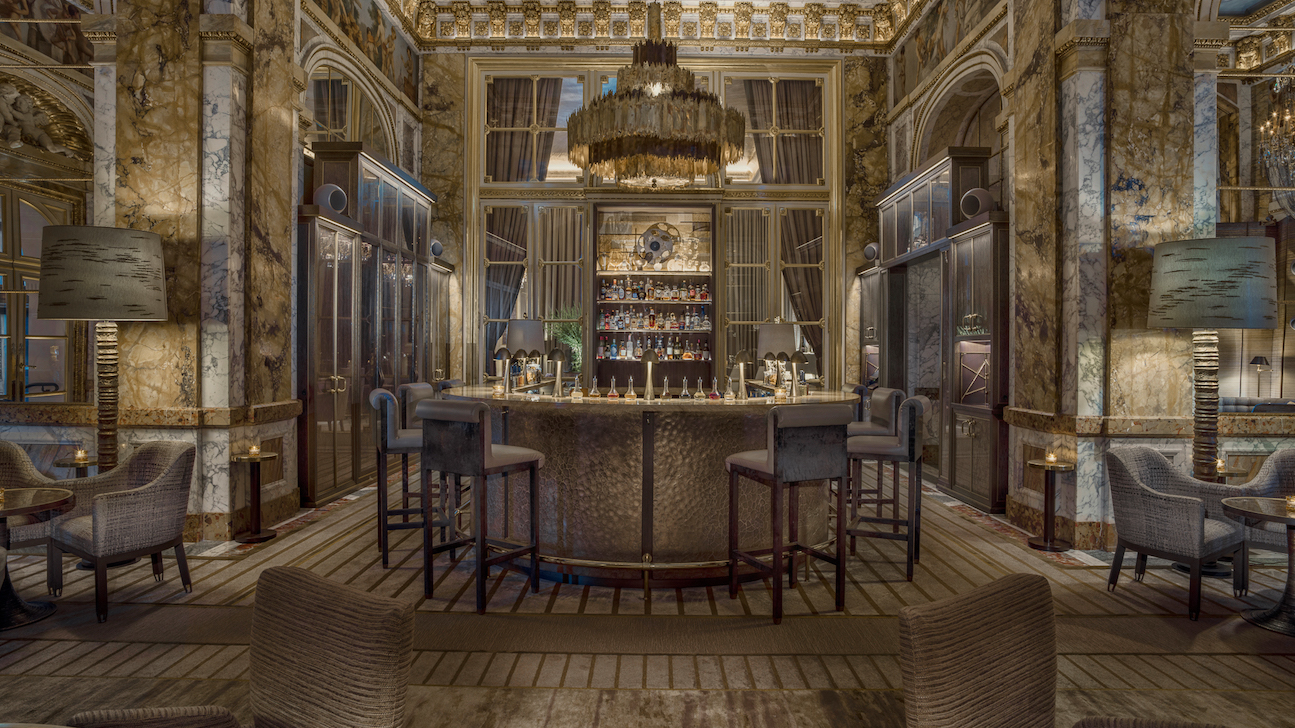Lounge and bar area at Les Ambassadeurs with marble walls, wooden floor, and cocktail bar and chair in the center.