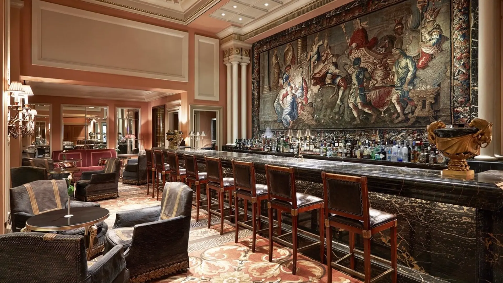 Pub and lounge with classical design, dark coloured furniture, marble pub table and a tapestry of Alexander The Great at the wall in Hotel Grande Bretagne