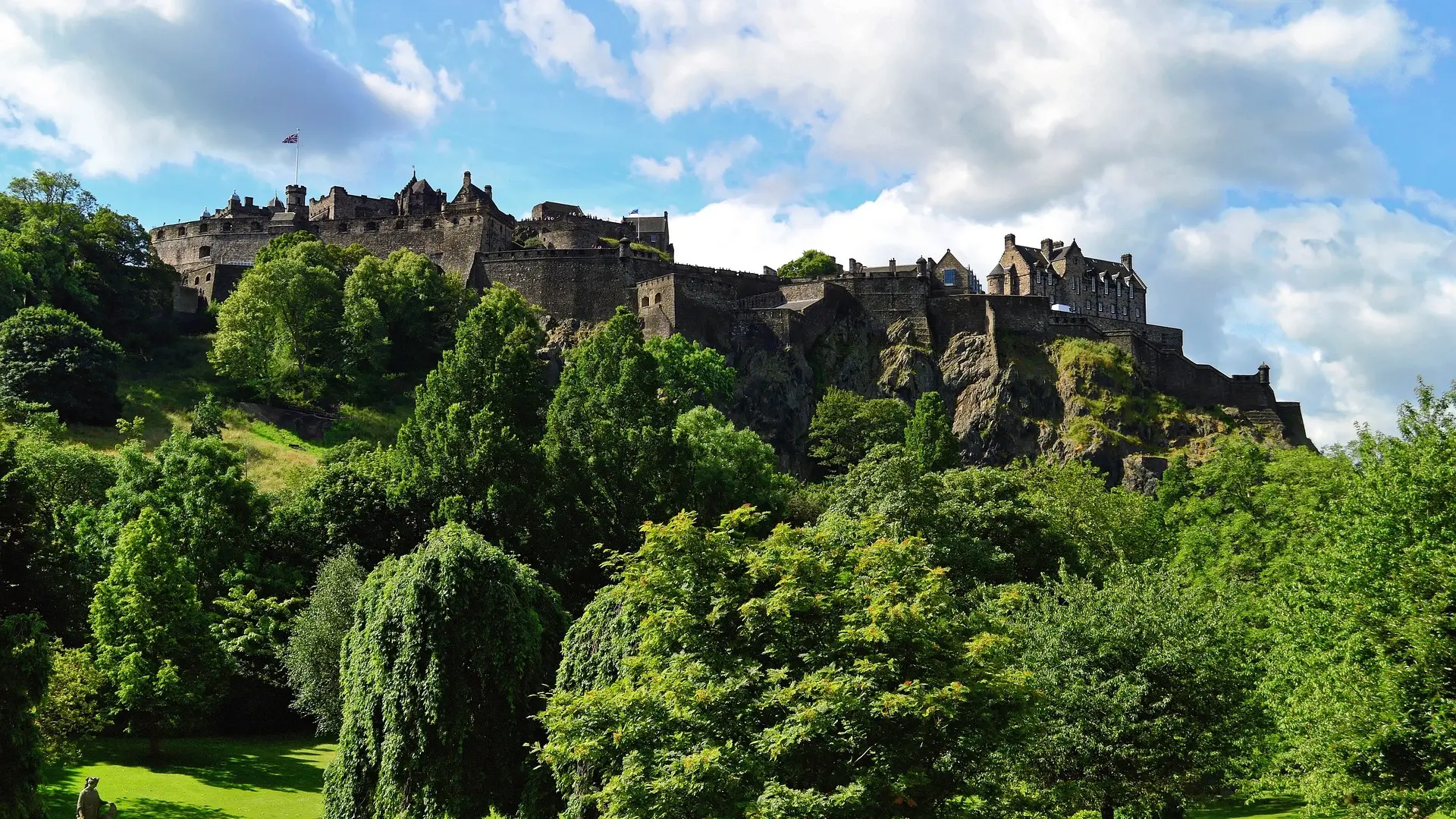 Green forest and at the top a massive black stone castle with a massive and tall battlements in Edinburgh, Scottand.