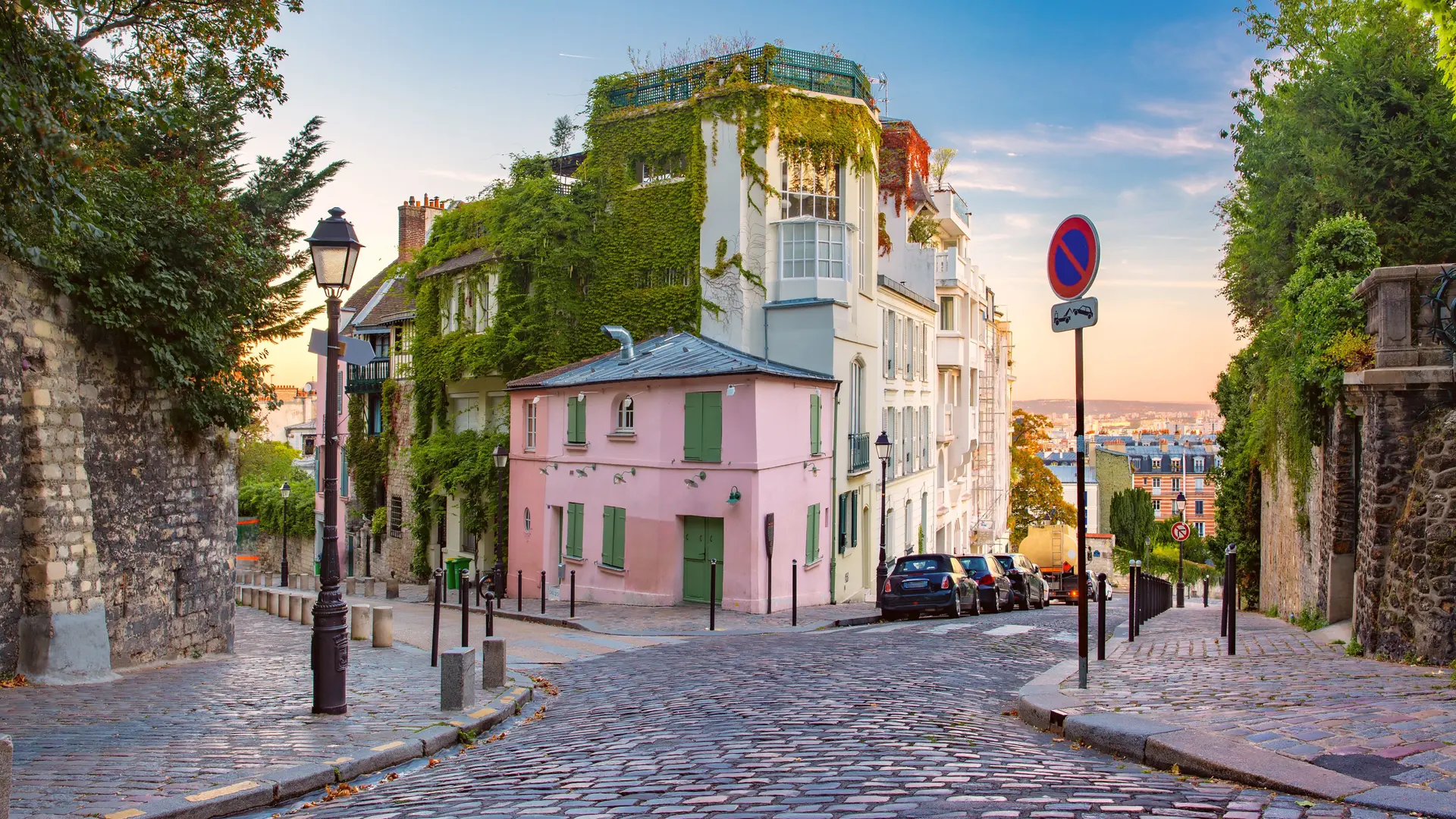 Lane in Paris with stone streets, pinkj and white building with green nature overtaken parts of it.