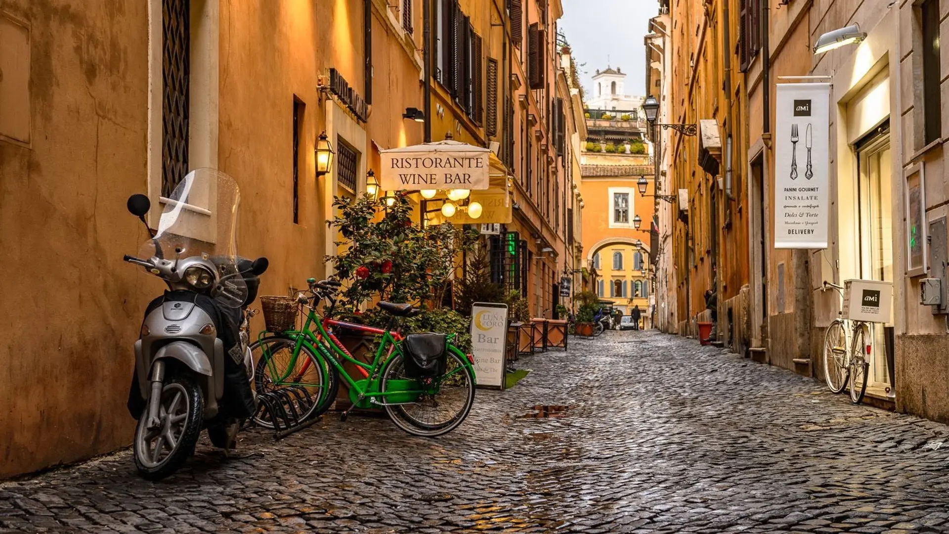 Small lane in Rome with bicycles and a motorbike, stone street, and orange sunset looking arcitecthure.