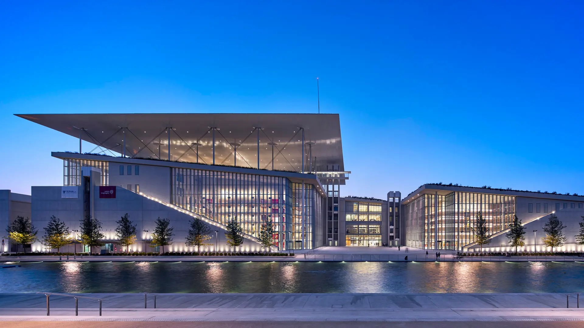 A modern cultural center by the water made of white stone with many glass windows.
