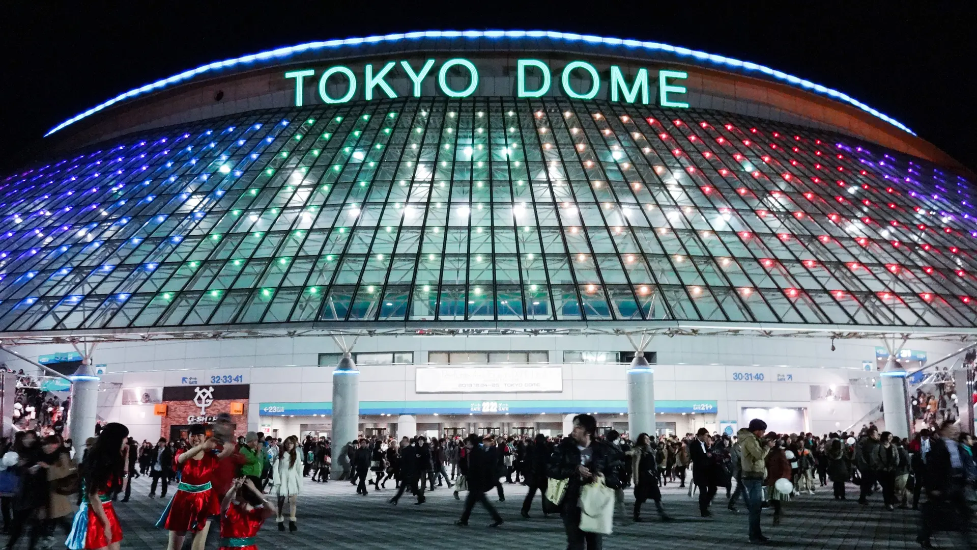 Large glass bowl lokking building with blue text saying: TOKYO DOME and crowded with people outside.